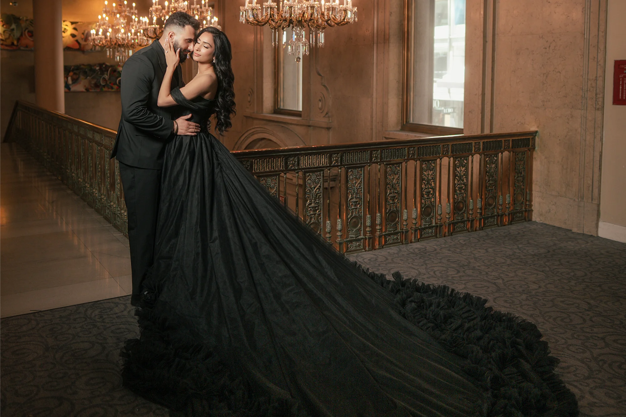Long Train Dress Rental black ruffled gown, couple embracing indoors under chandeliers